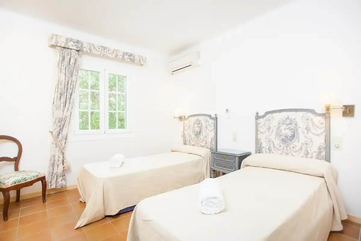 A bright bedroom with two beds, patterned headboards, and a window.