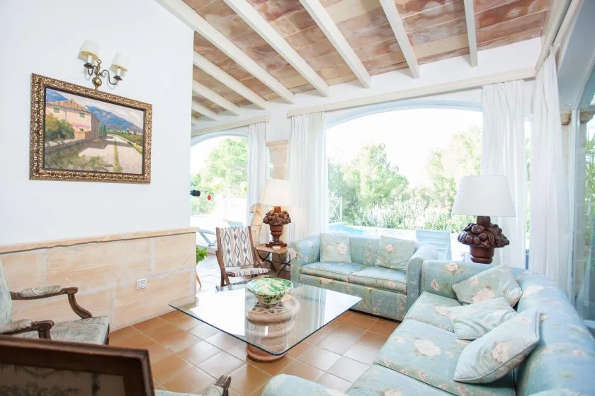 A bright living room with pale seating and large windows overlooking greenery.