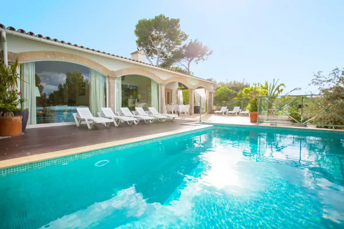 A swimming pool beside a house with arched windows and lounge seating.