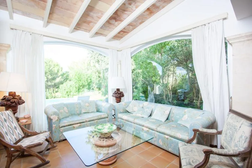 A bright sunroom with pale seating and large windows overlooking greenery.