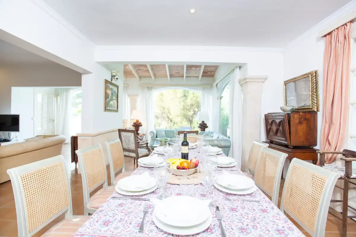 A dining room with a long table set with plates and surrounded by chairs.