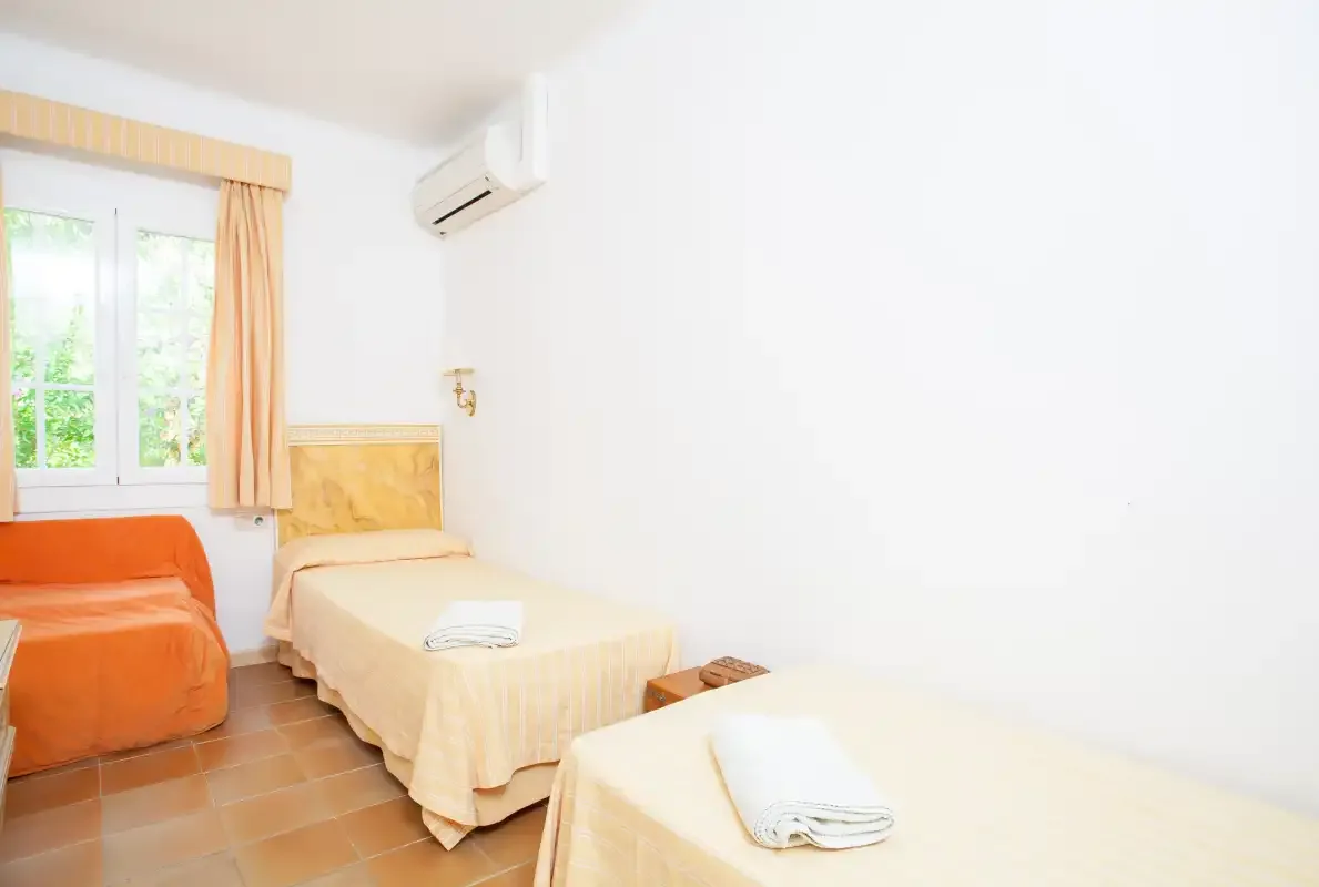 A bedroom with two beds, an orange armchair, and a curtained window.