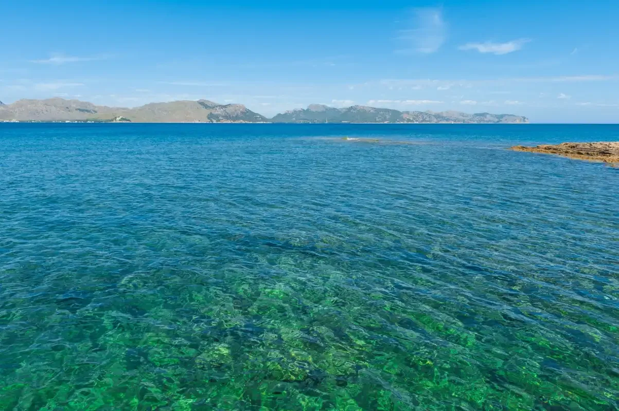 Clear blue sea stretches toward a distant mountainous coastline.