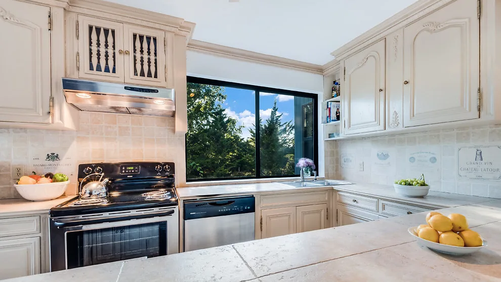 Una cocina luminosa con gabinetes color crema, una estufa y una gran ventana con árboles.