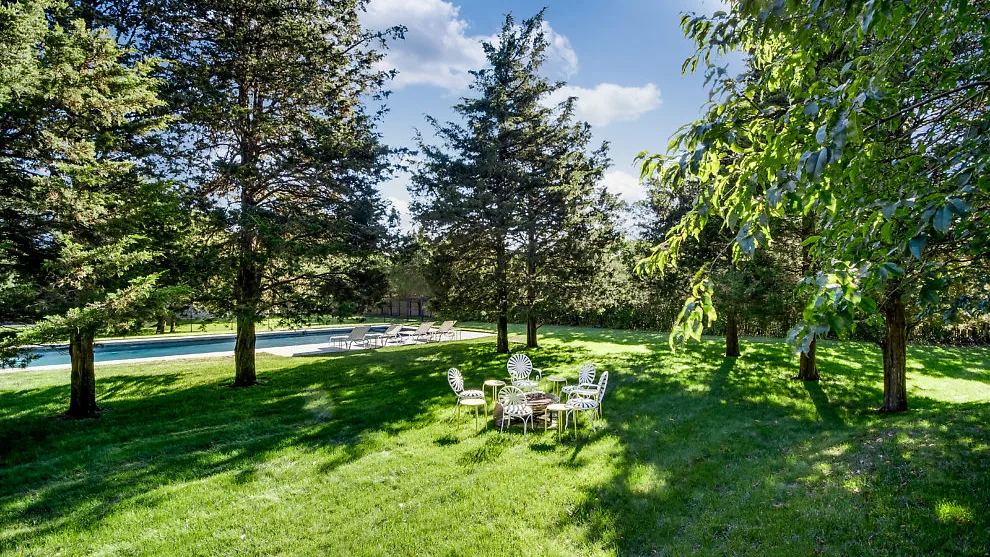 A grassy garden with outdoor seating beneath leafy trees.