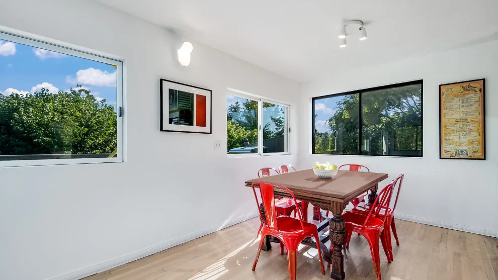 Una luminosa zona de comedor con mesa de madera y asientos rojos junto a grandes ventanas.