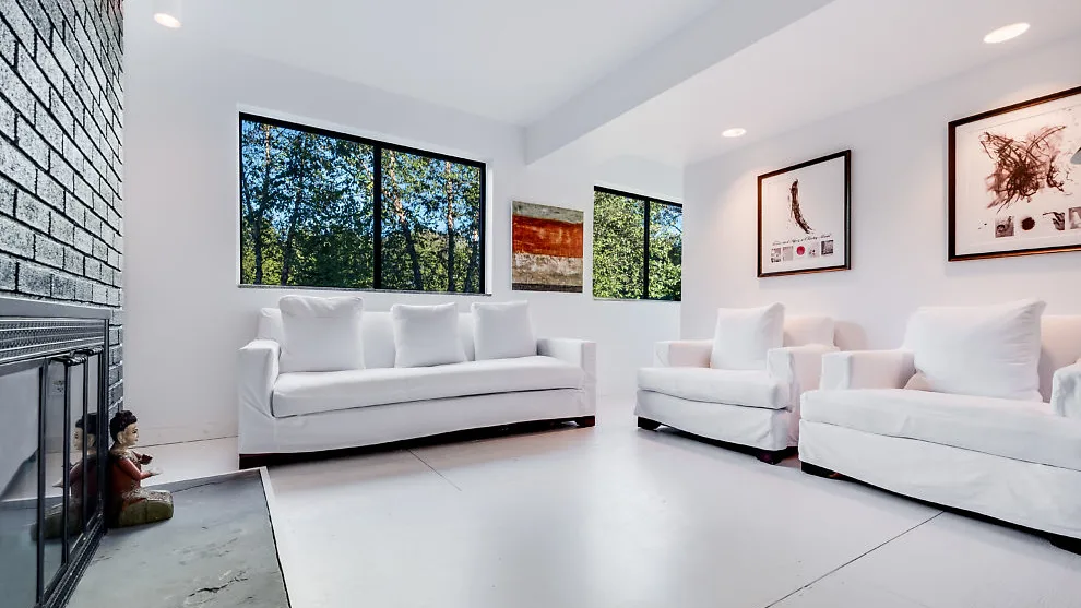 Una sala luminosa con asientos blancos, ventanas grandes y cuadros en las paredes.