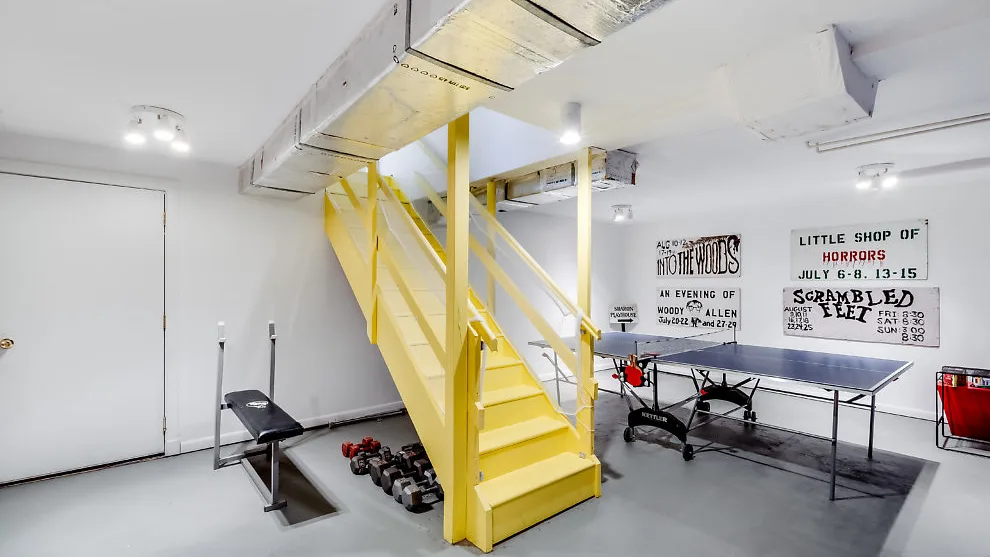 Una zona recreativa interior luminosa con escaleras amarillas y equipo de ejercicio.