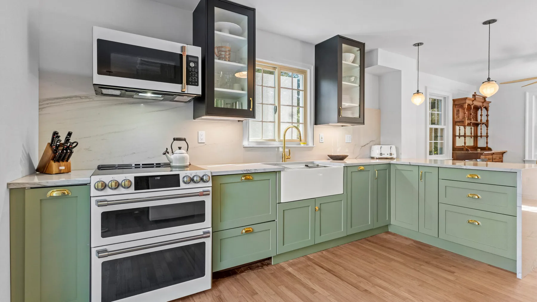 A bright kitchen with green cabinets, a range, and a central sink.