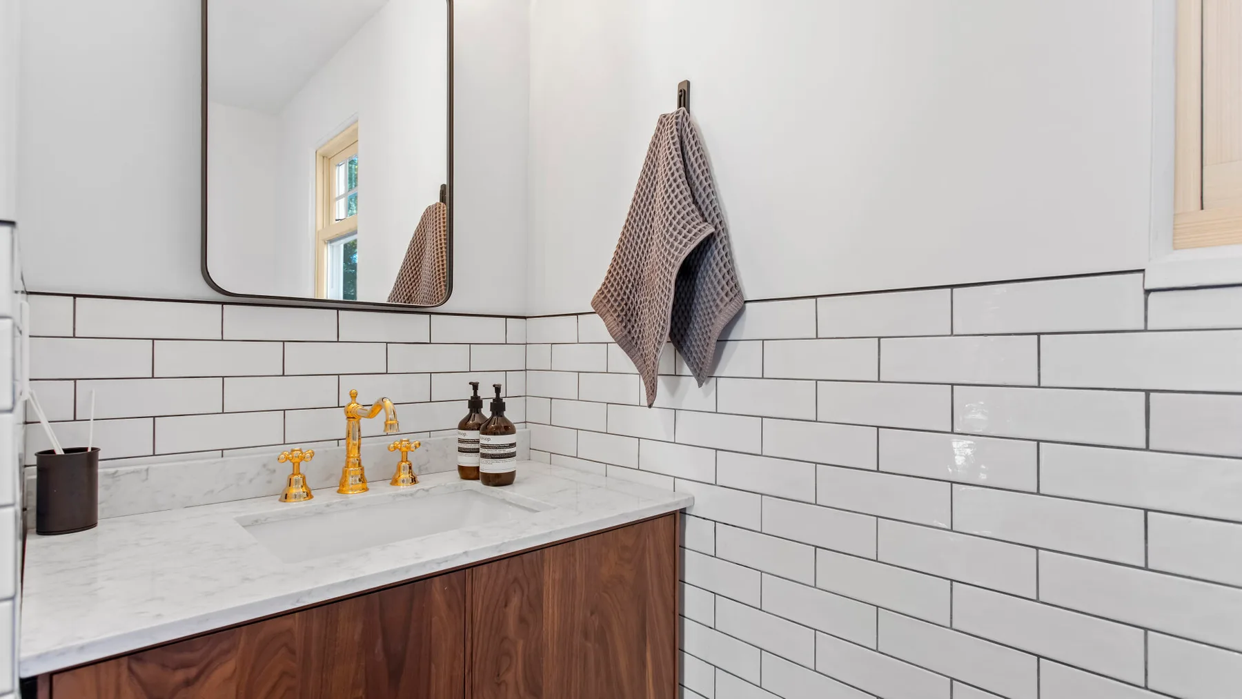 A bathroom vanity with a white countertop and tiled walls.