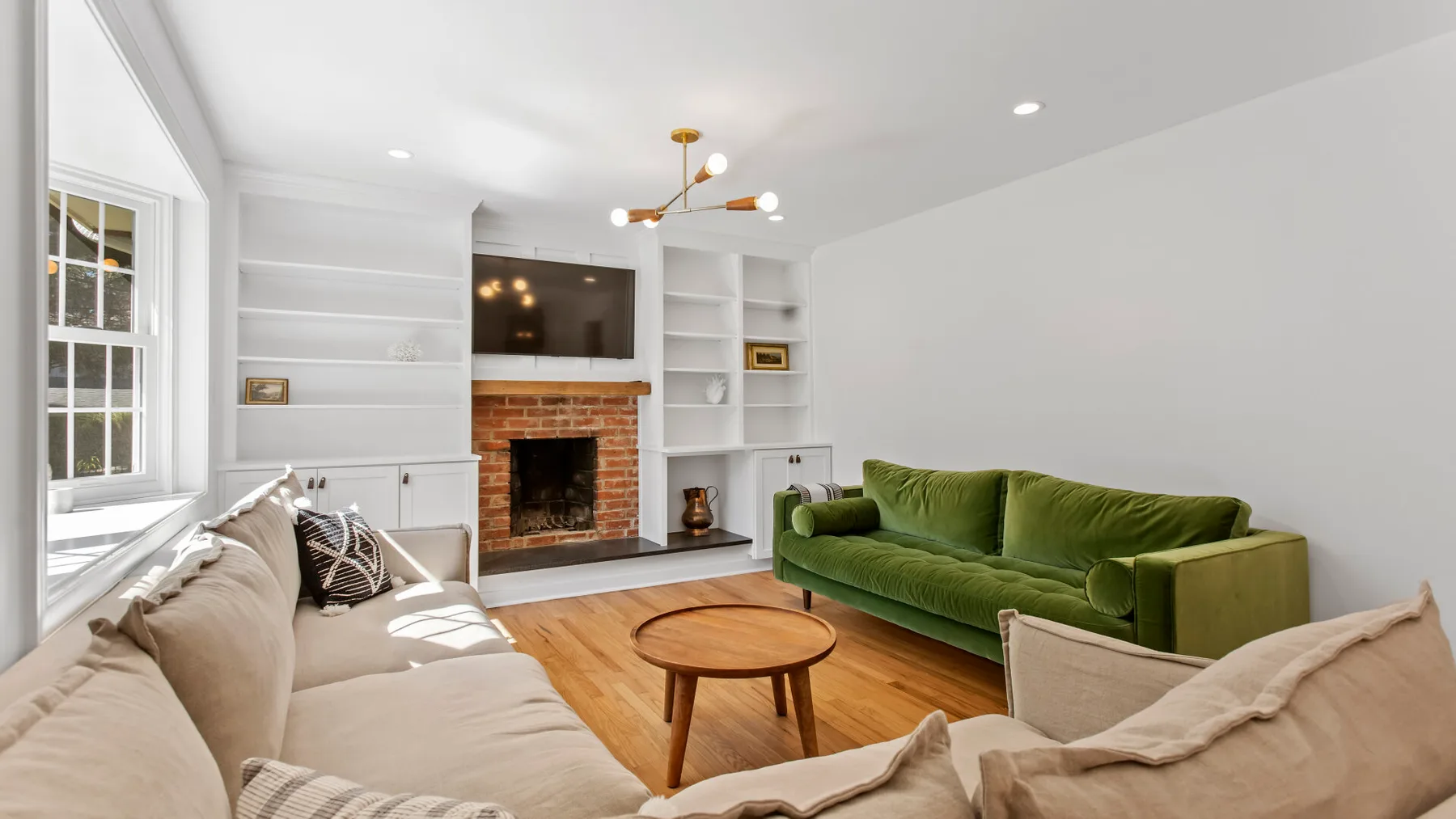 Una sala luminosa con un sofá verde, asientos beige y una chimenea de ladrillo.