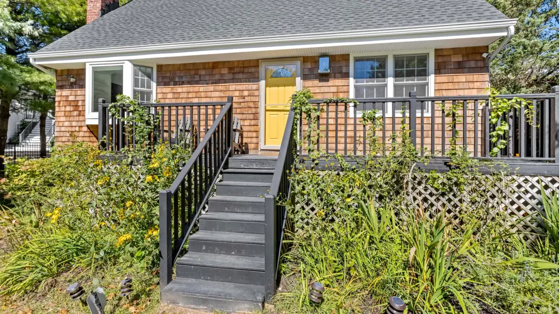 A house exterior with a yellow front door, raised deck, and stairs.