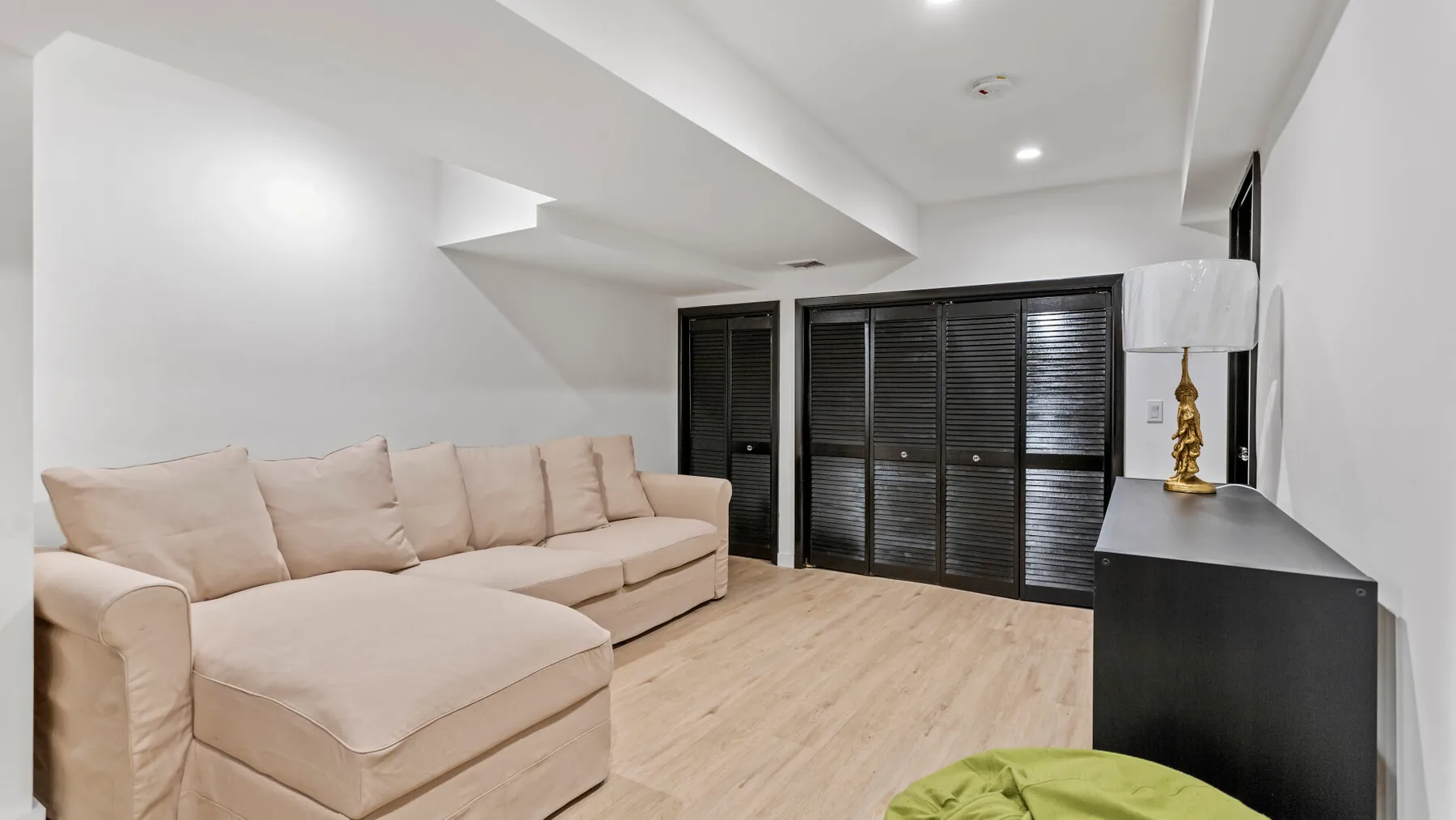 A bright living room with pale seating and dark louvered doors.