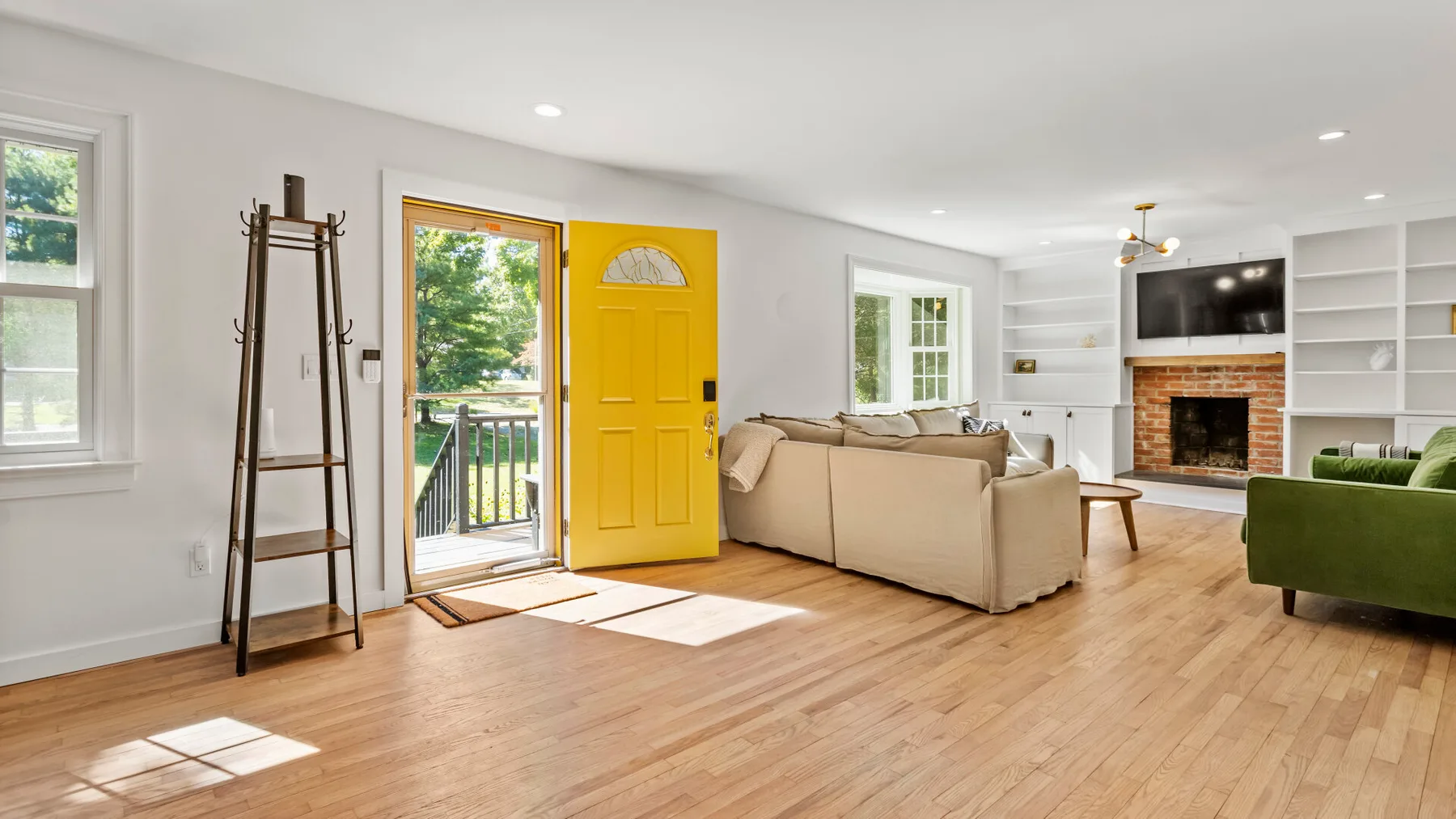 A bright living room with light seating, built-in shelves, and a brick fireplace.