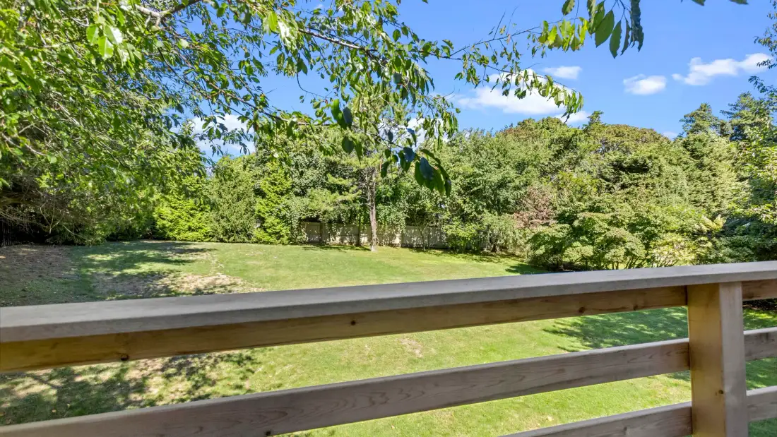 A wooden railing overlooks a grassy outdoor area surrounded by trees.