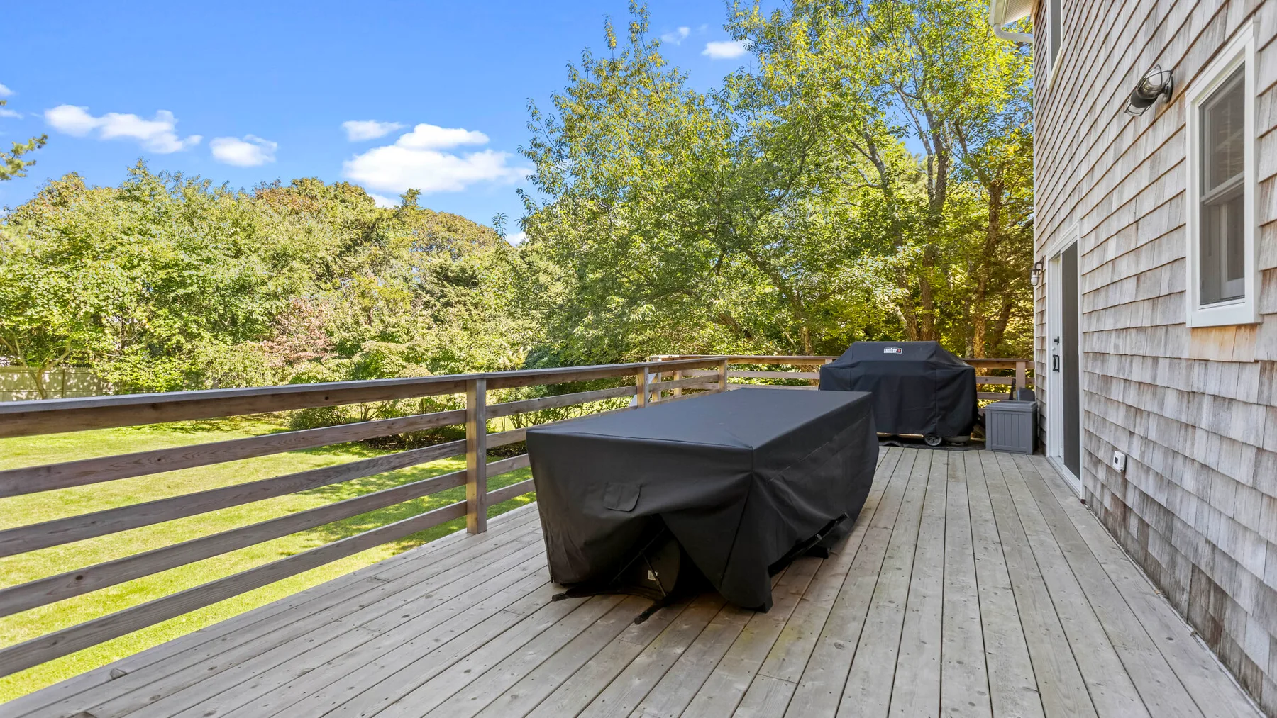 An outdoor deck has a covered table and grill beside a house.