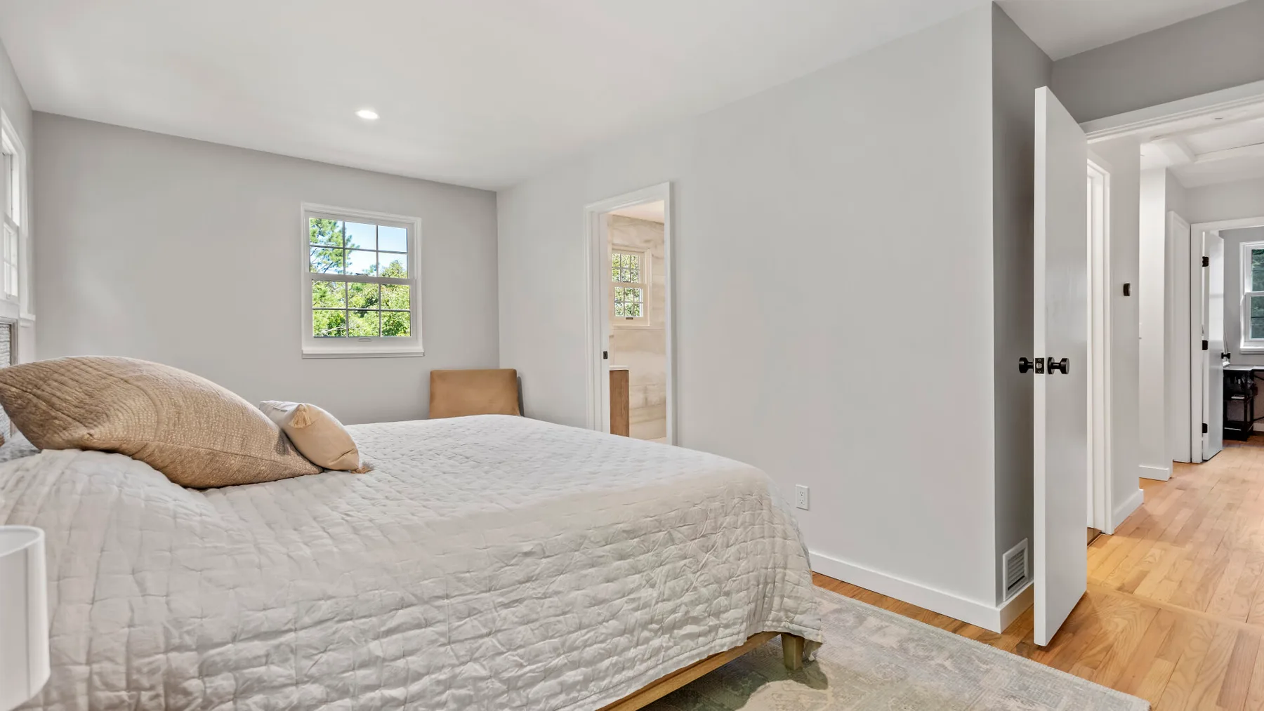 A bright bedroom with a large bed, a window, and an open doorway.