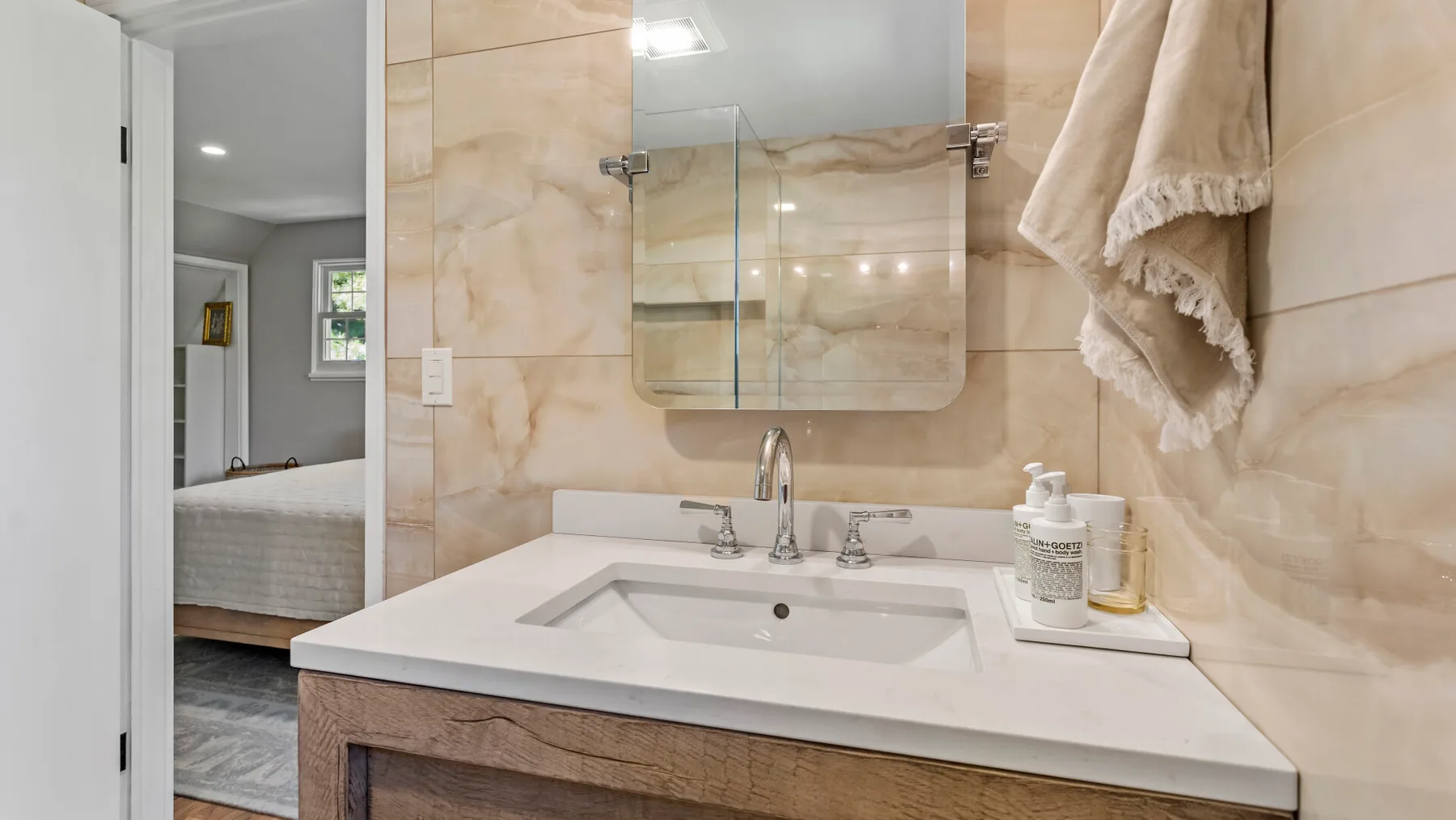 A bathroom vanity with a sink and mirror beside an open doorway to a bedroom.
