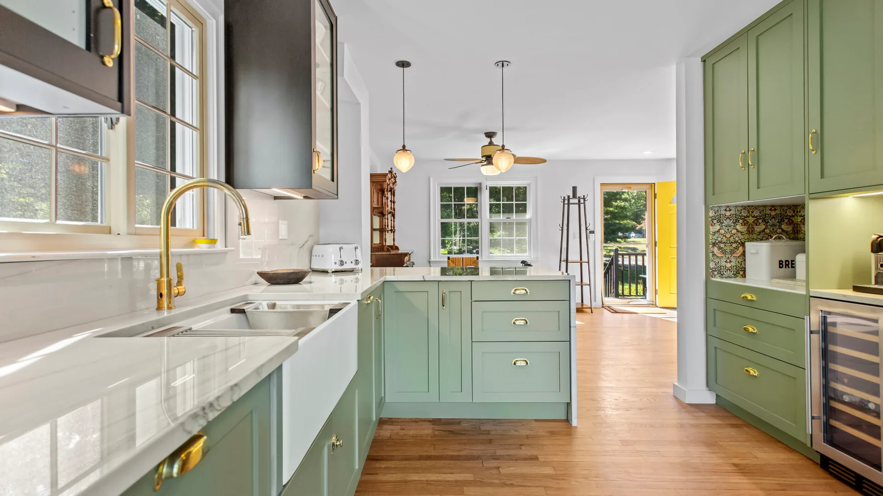 A bright kitchen with green cabinetry, white counters, and windows overlooking the outdoors.