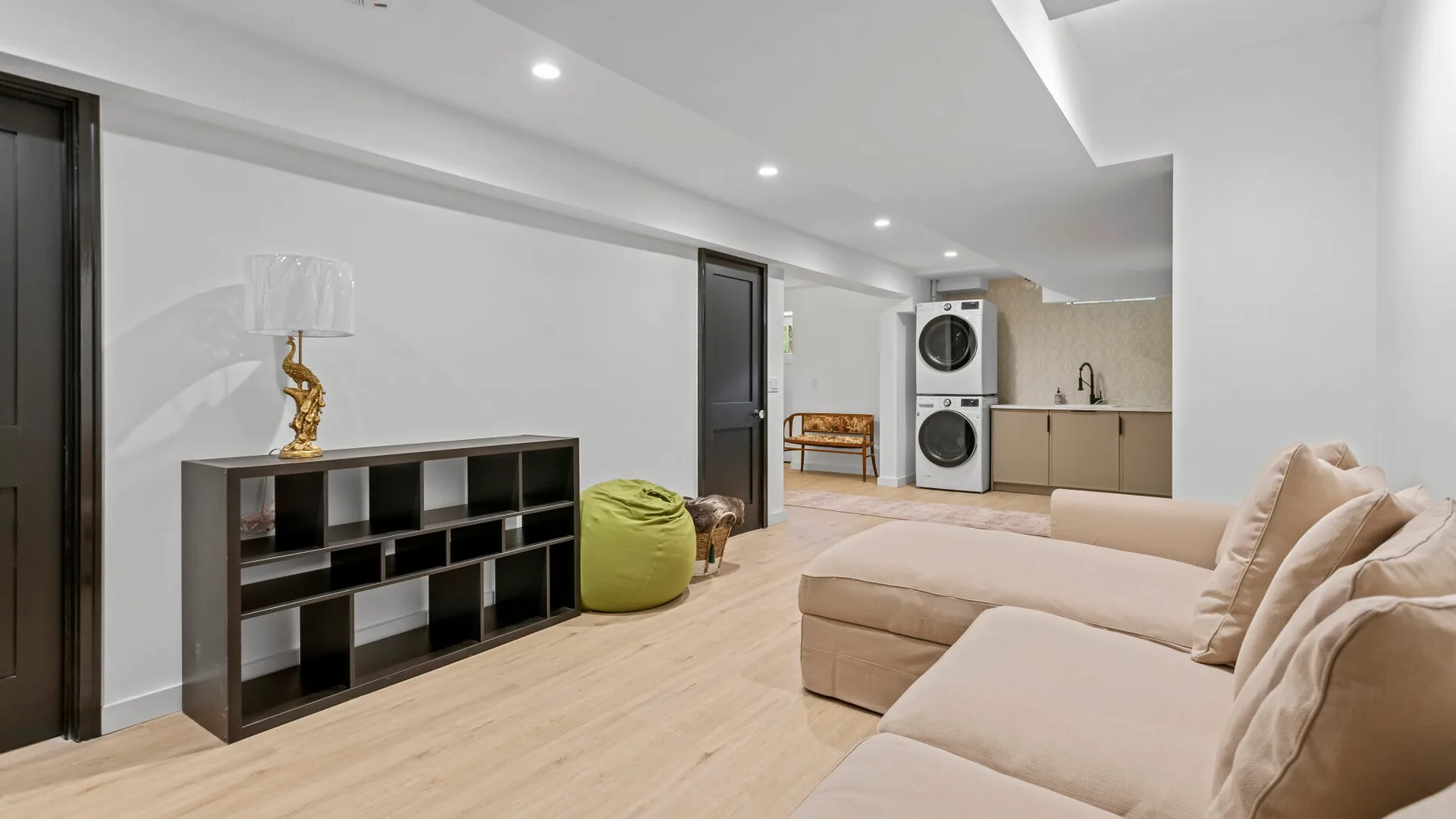 A bright living room with beige seating and a black shelving unit.