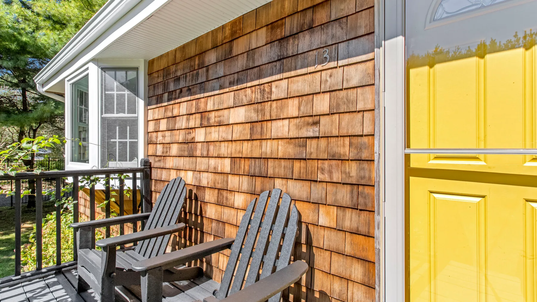 A wooden porch with two chairs beside a bright yellow door.