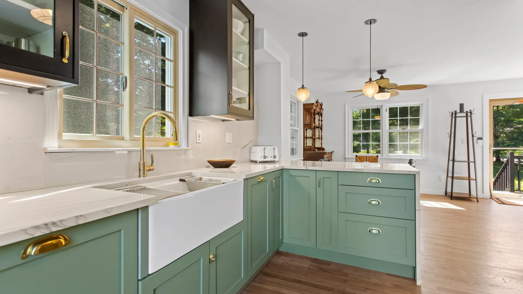 A bright kitchen with green cabinets, a sink, and windows overlooking a living area.