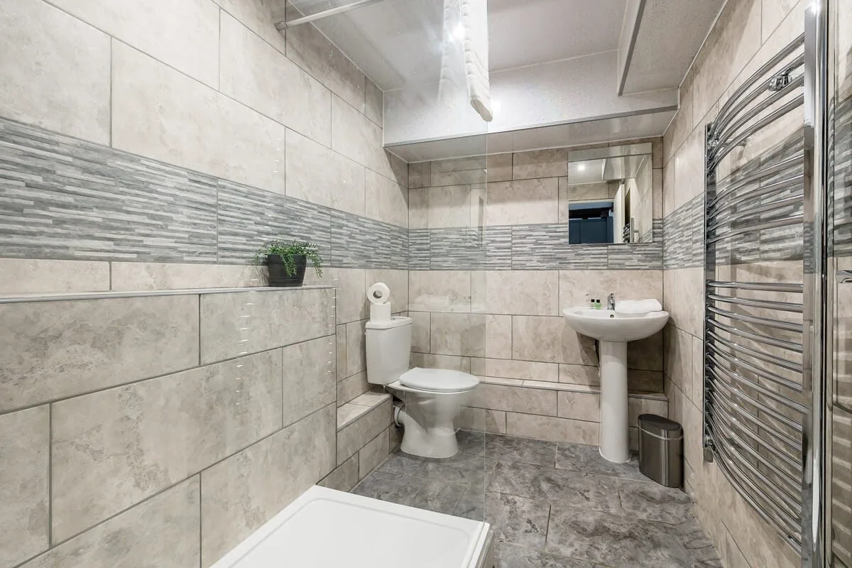 Un baño alicatado con inodoro, lavabo con pedestal y toallero calefactable.