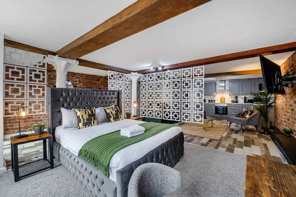 Dormitorio con una cama grande y un separador estampado que da a una cocina.
