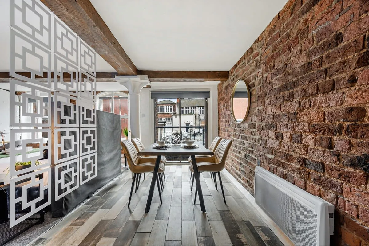 Comedor con una mesa y sillas junto a una pared de ladrillo visto.