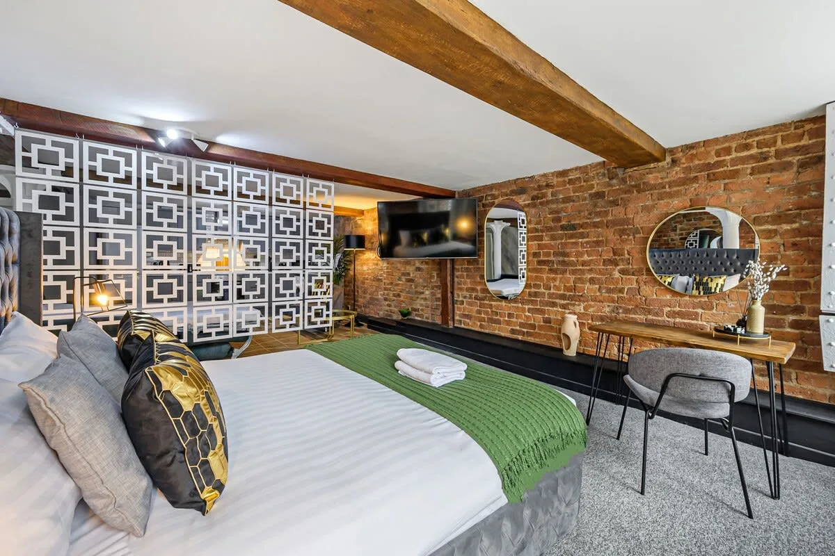 Dormitorio con cama, paneles decorativos estampados y escritorio junto a una pared de ladrillo.