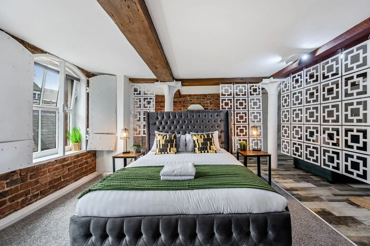 Un dormitorio con una cama grande, paneles decorativos en la pared y vigas de madera a la vista.