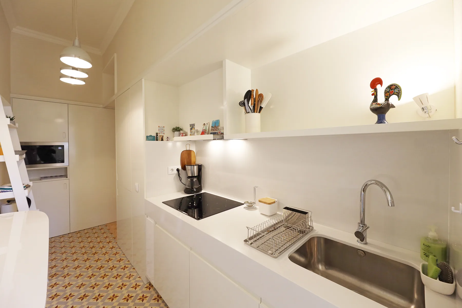 Una cocina luminosa con encimeras blancas, fregadero y placa de cocina.