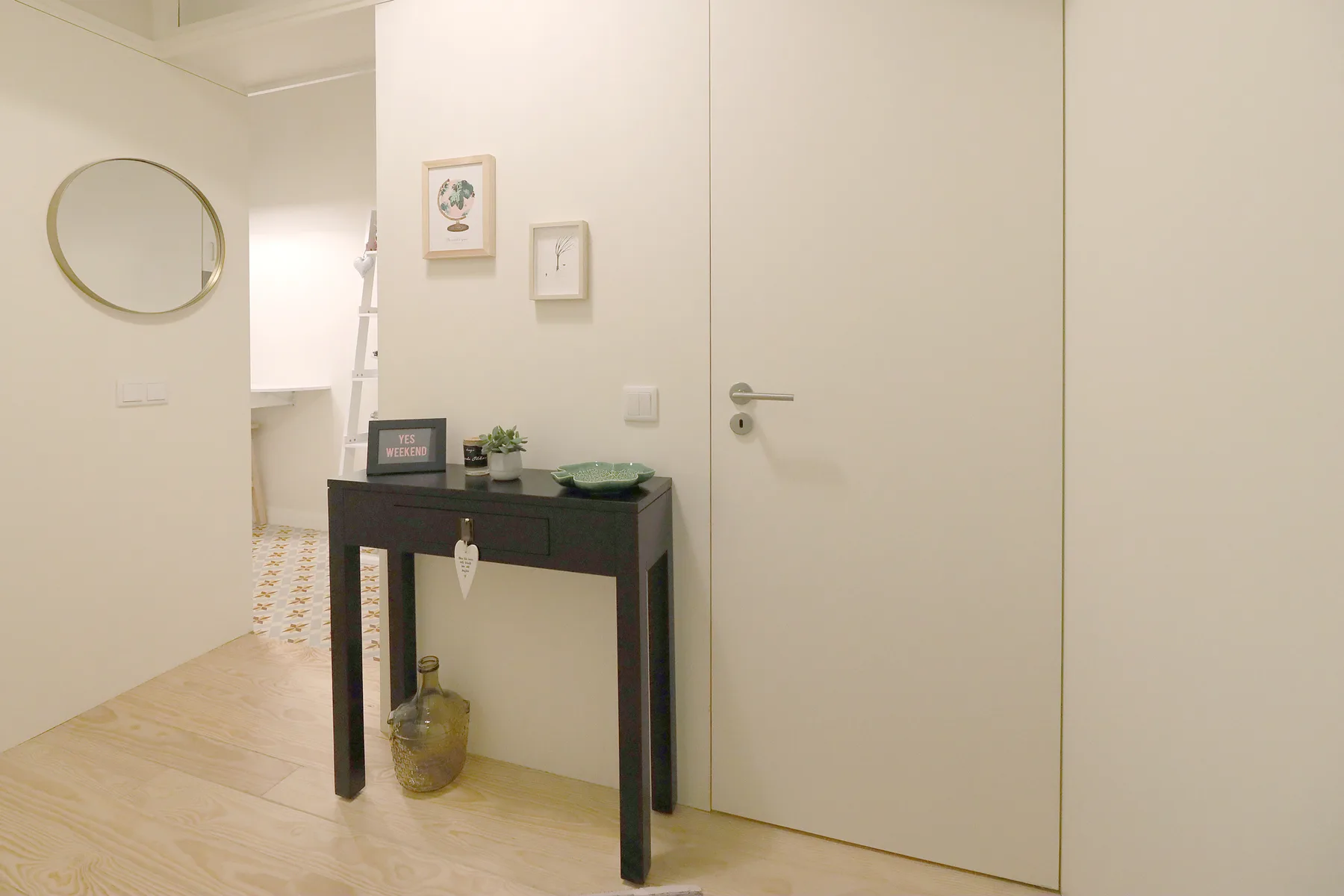 La entrada de un apartamento tiene una consola estrecha debajo de dos cuadros pequeños.