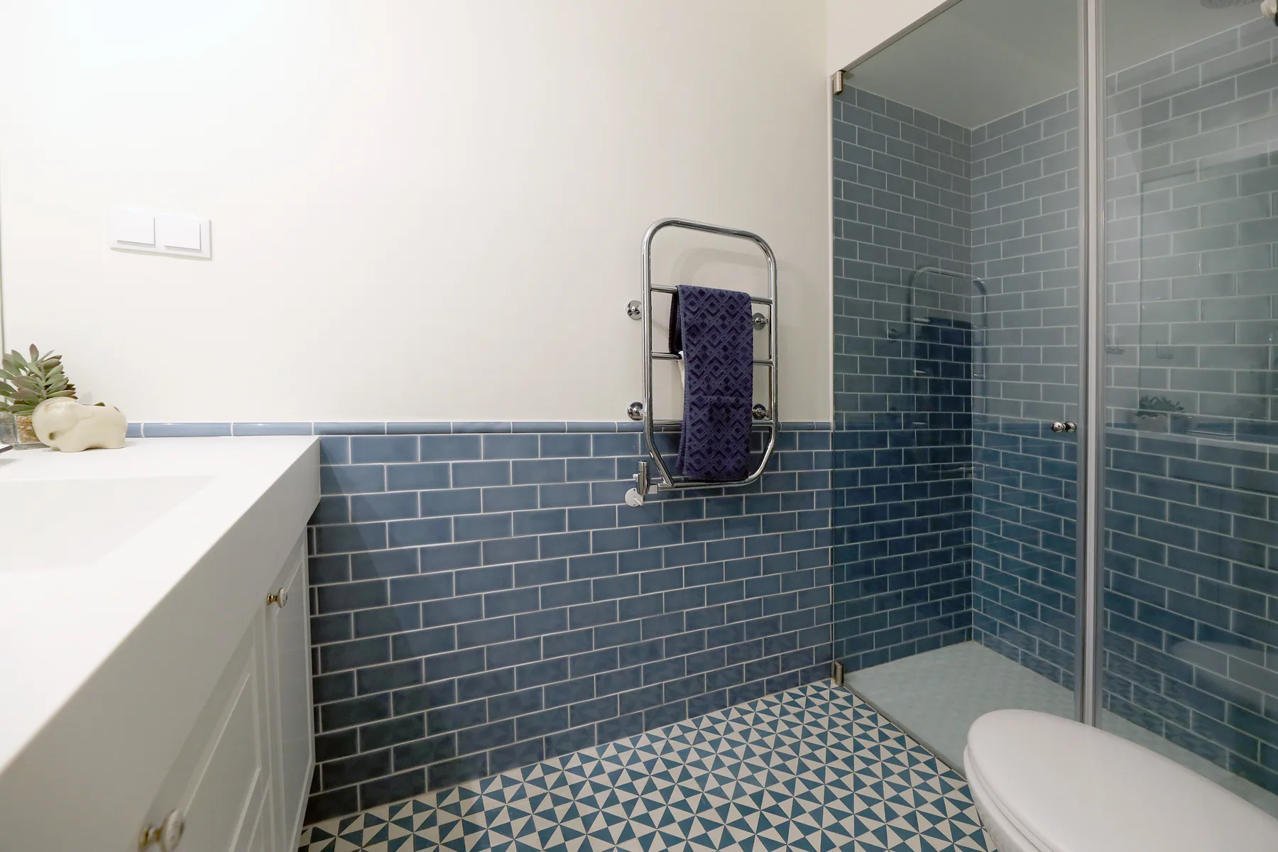 Un baño con paredes de azulejos azules, una ducha de vidrio y un lavabo blanco.