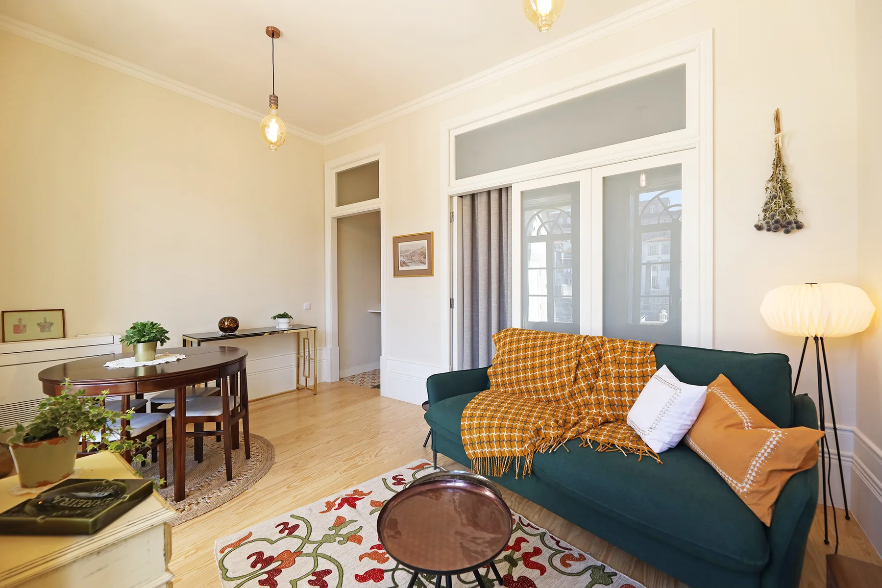 Una sala de estar con un sofá verde azulado, una manta estampada y ventanas grandes.
