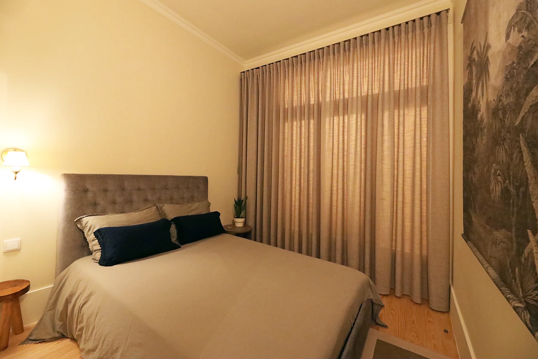 Un dormitorio con una cama, una lámpara de noche y cortinas largas.