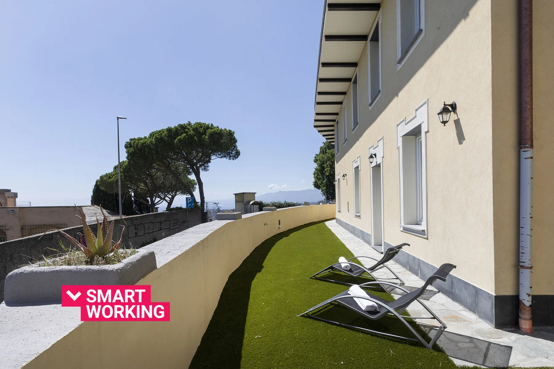 Una terraza en la azotea con asientos reclinables y una franja de césped artificial junto al edificio.