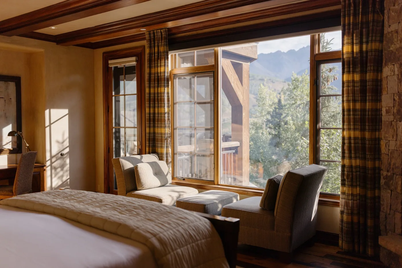 A bedroom with a bed and seating beside large windows overlooking trees and mountains.