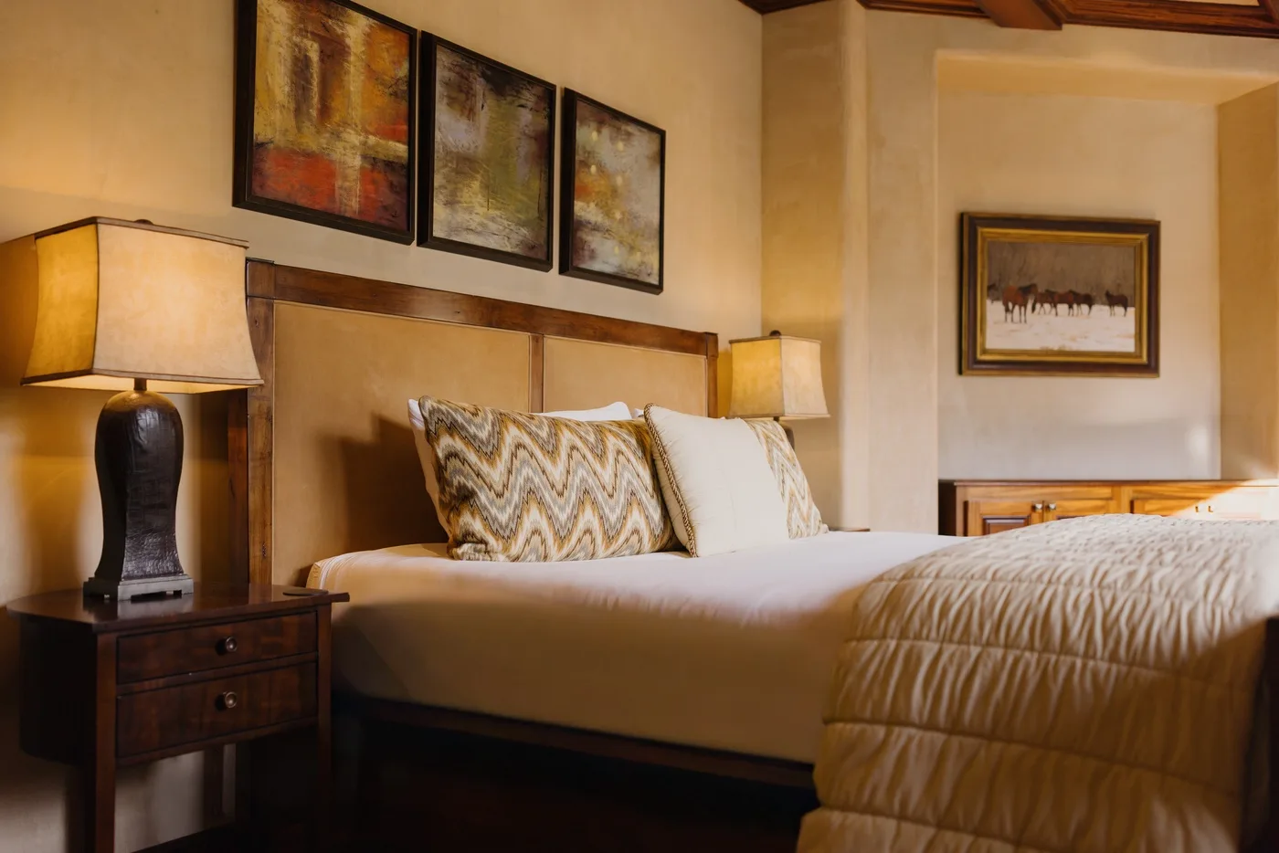 A bedroom with a neatly made bed, patterned pillows, and framed artwork.