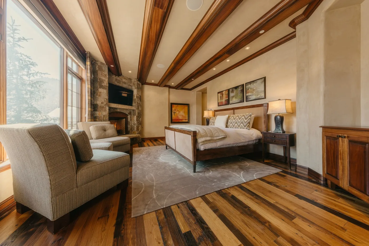 A bedroom with a large bed, lounge seating, and exposed wooden ceiling beams.