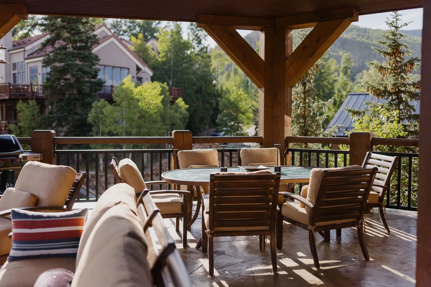 A covered outdoor seating area with a dining table overlooks trees and nearby houses.