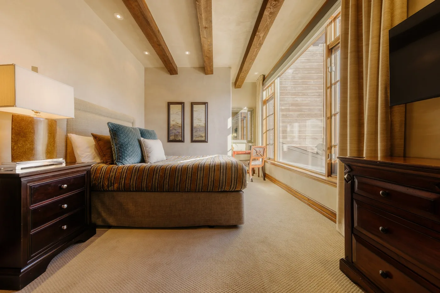 A bedroom with a bed beside large windows and a television.