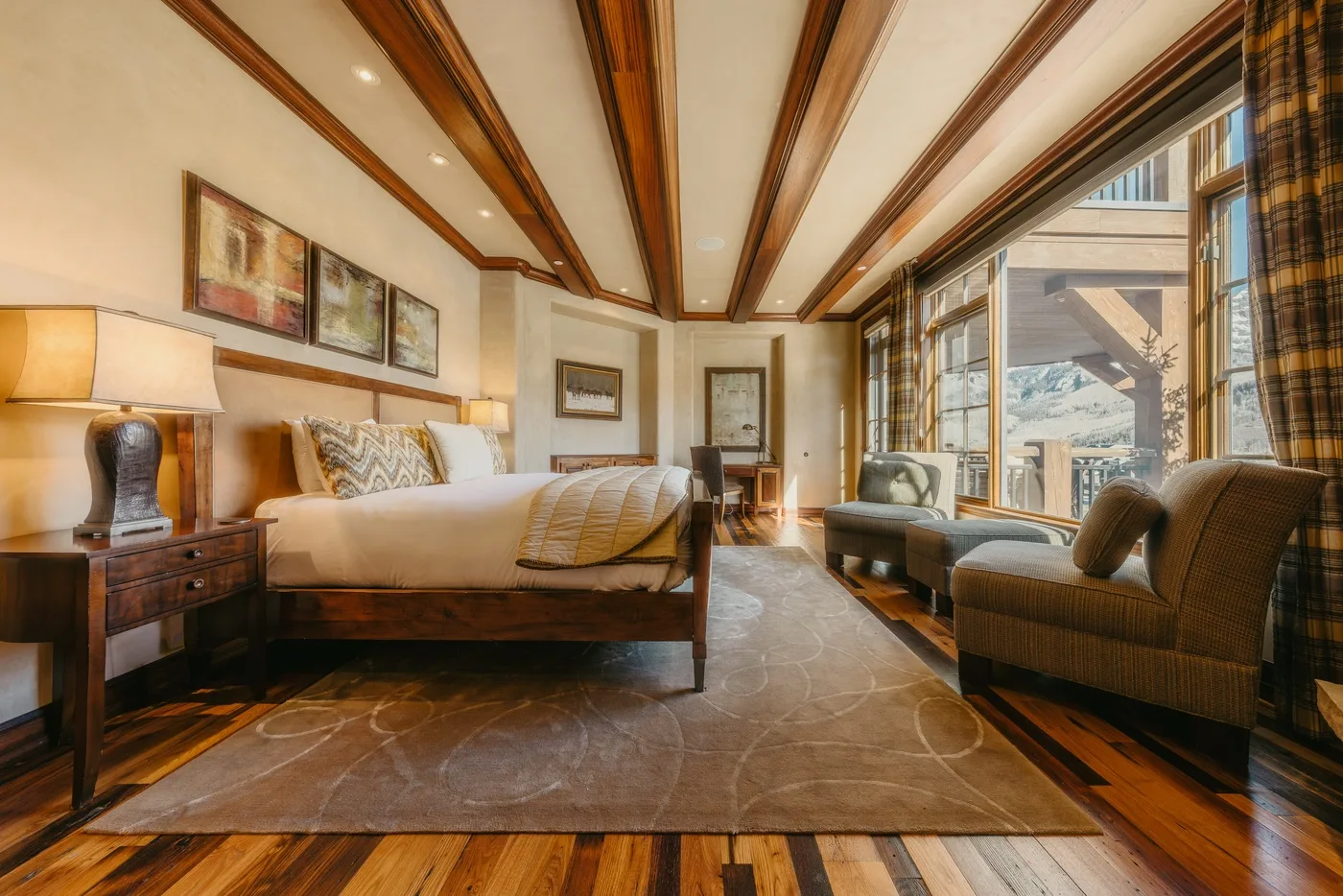 A bedroom with a large bed and seating beside broad windows.
