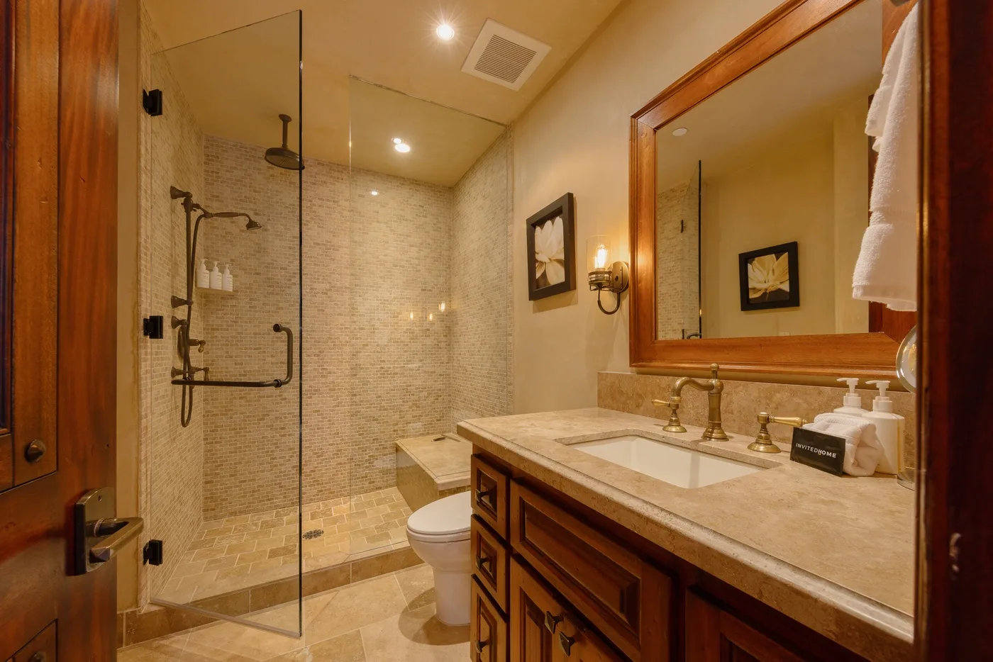 A bathroom with a glass shower, toilet, and wood vanity.