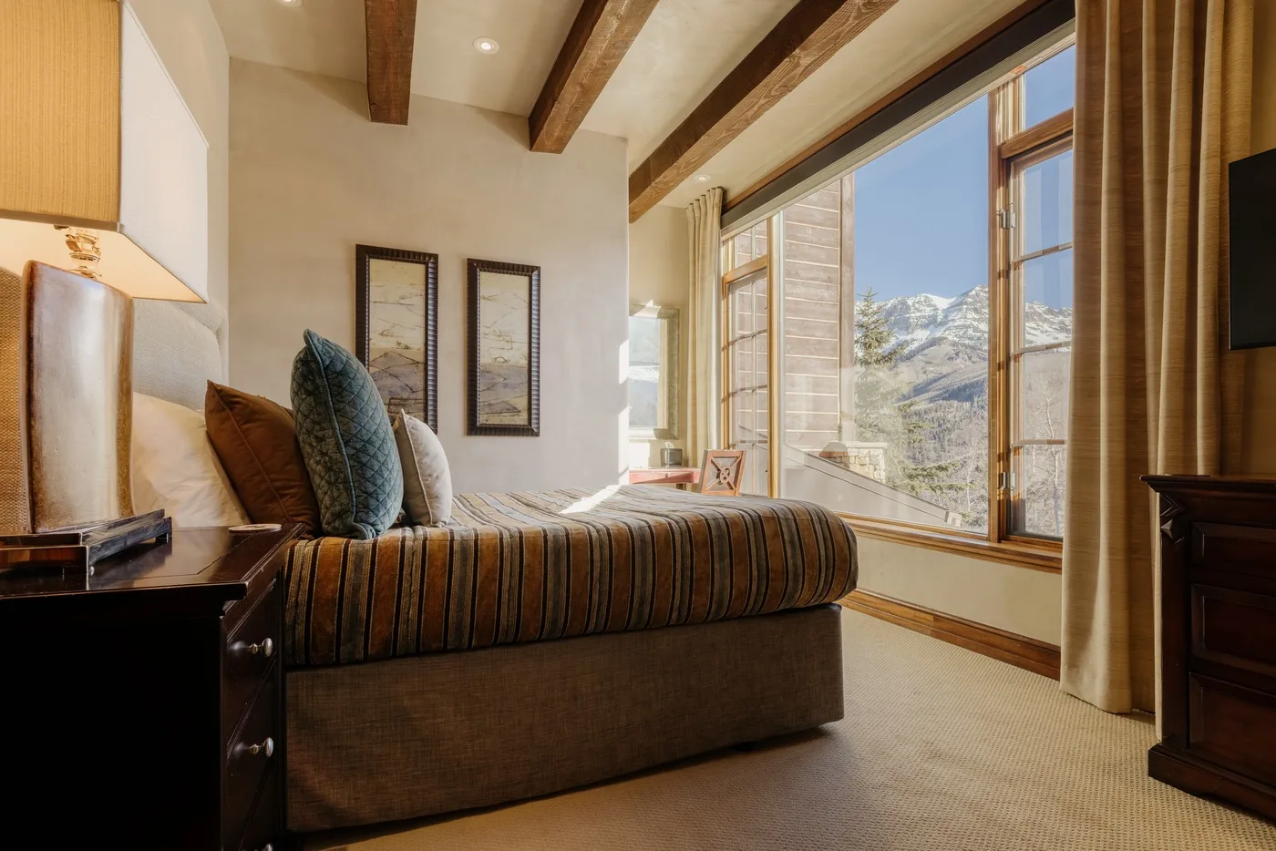 A bedroom with a bed beside large windows overlooking a mountain landscape.