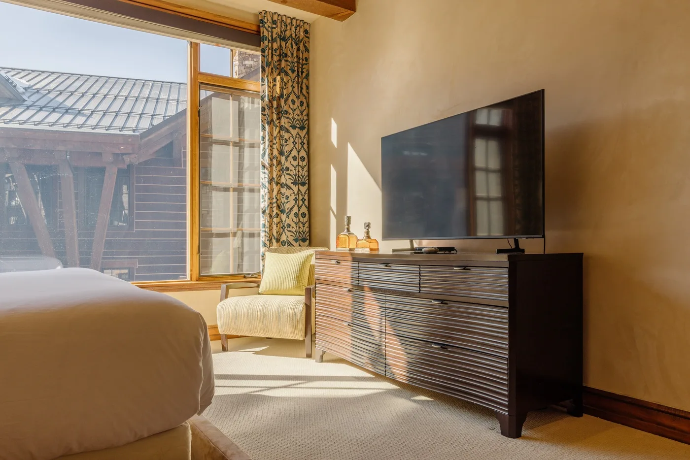A bedroom with a bed, a lounge chair, and a television on a dresser.