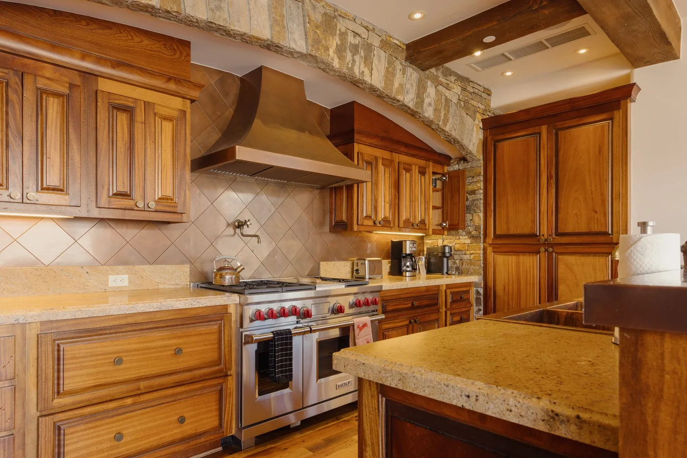 A rustic kitchen with wooden cabinets, a stainless steel stove, and a stone-topped island.