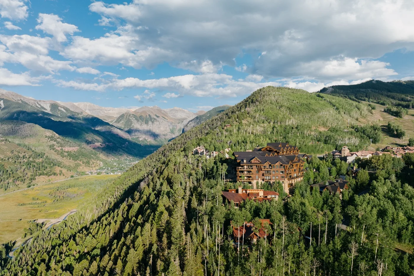 A mountain resort sits among forested hills beneath a partly cloudy sky.