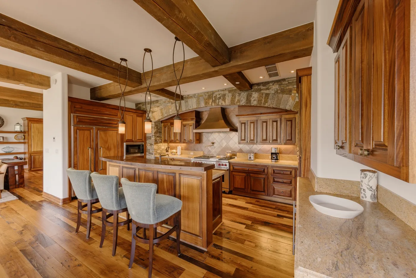 A spacious kitchen with a central island, wooden cabinets, and exposed ceiling beams.