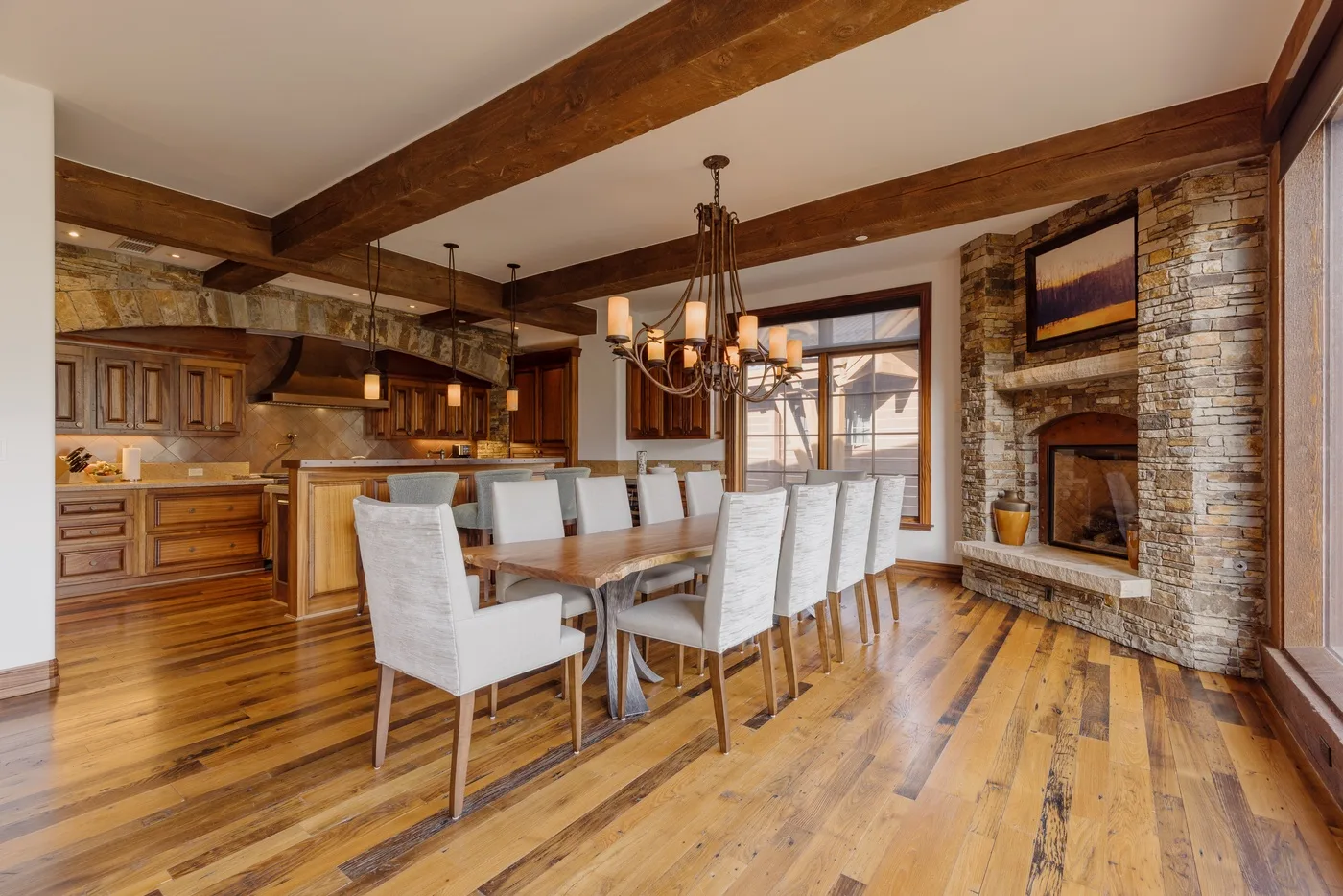 An open dining area and kitchen with a table beside a stone fireplace.